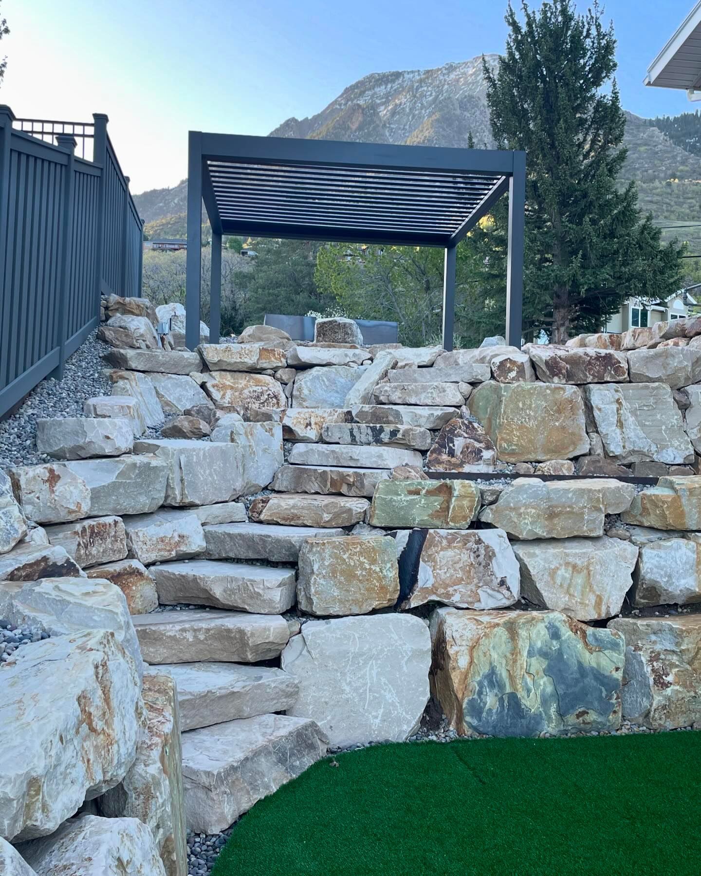 A stone wall with stairs and a pergola in the background.