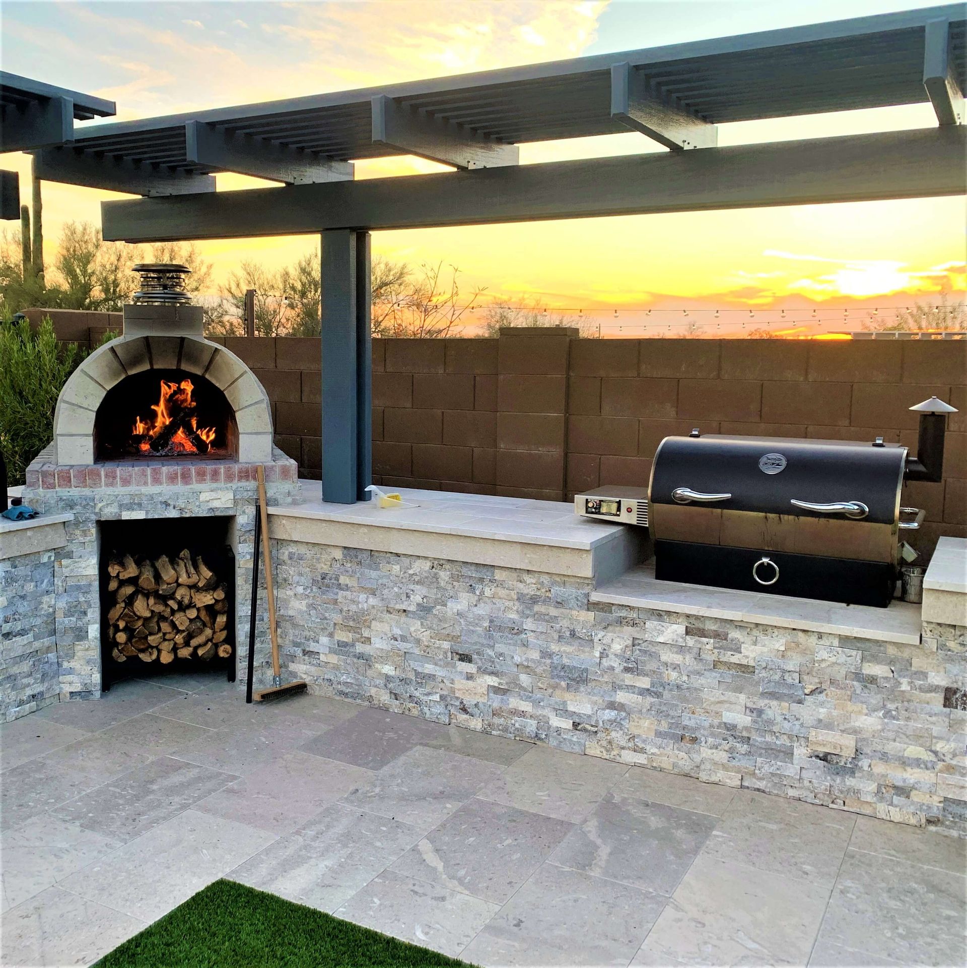 A pizza oven is sitting under a pergola next to a grill.