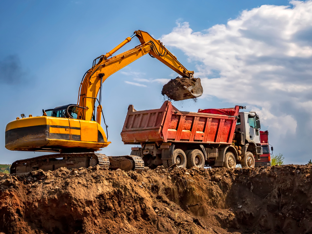 A yellow excavator is loading dirt into a red dump truck.