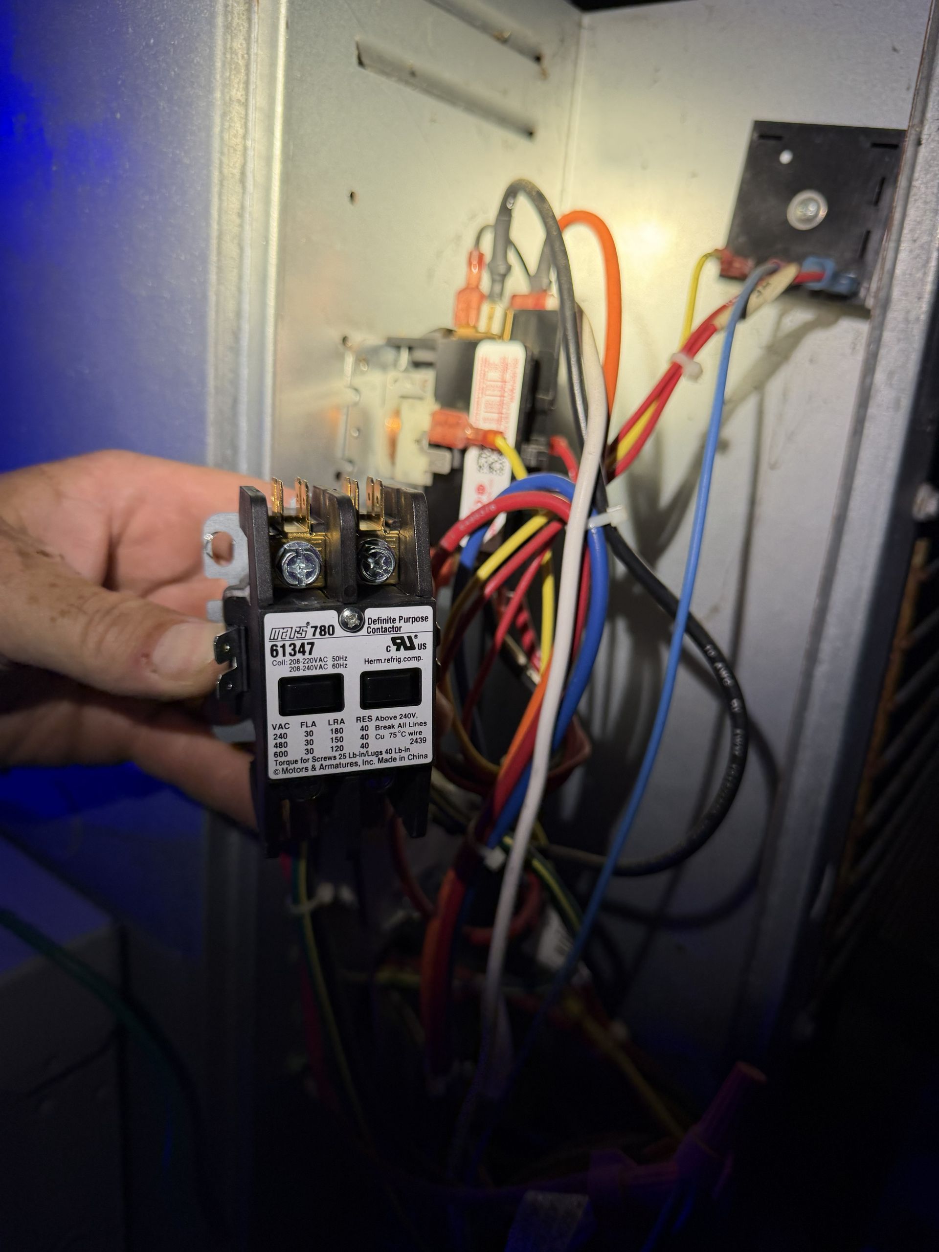 Hand holding an electrical relay panel with multicolored wires inside an open wall box