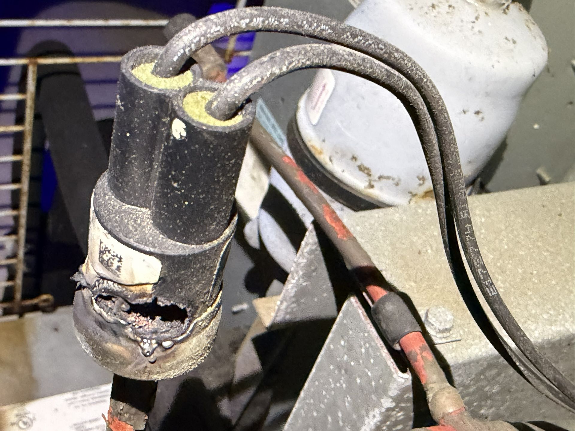 Close-up of a damaged black electrical connector with exposed wires on machinery.