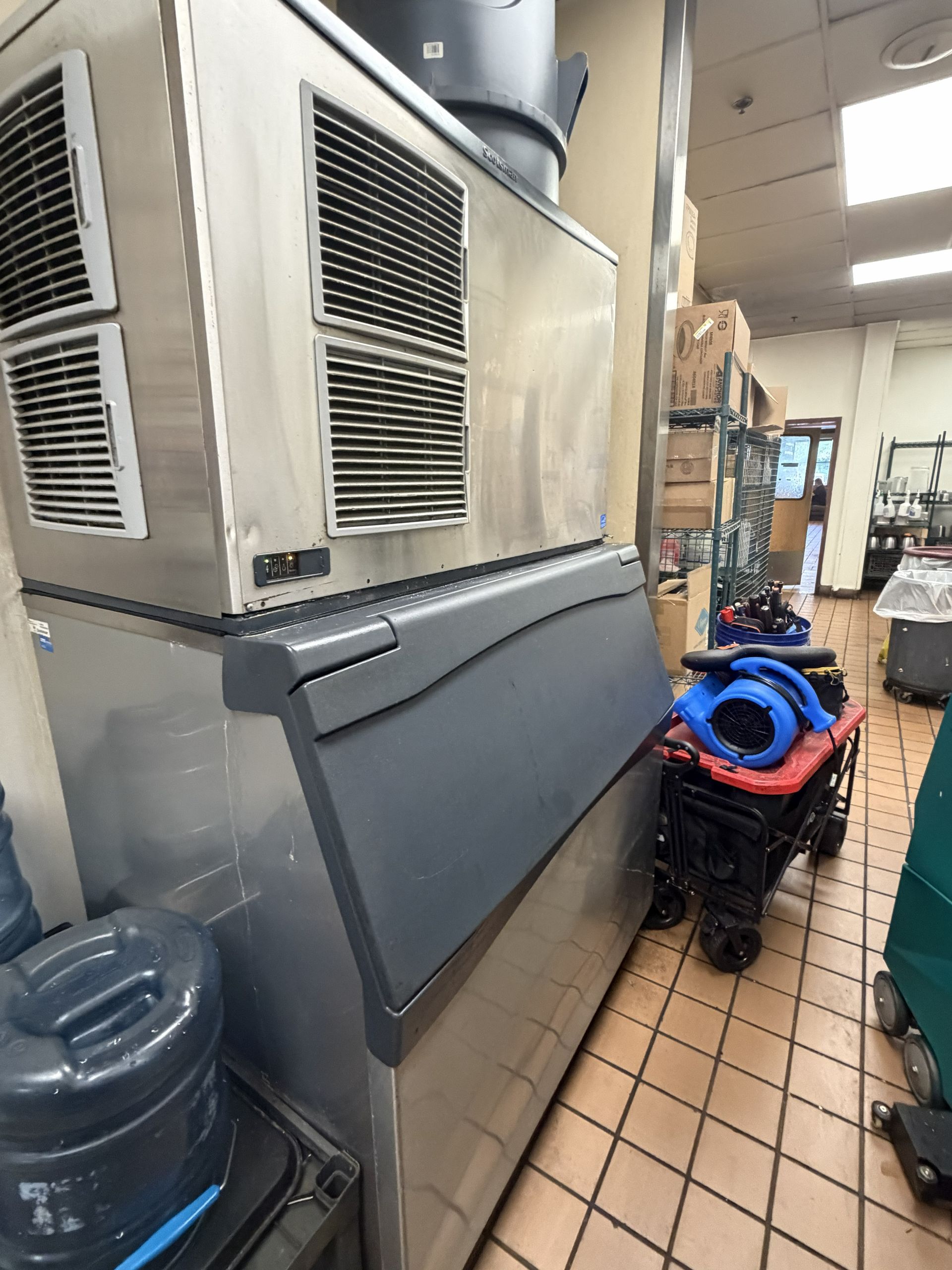 Industrial HVAC units in a narrow utility hallway with a blue coiled hose cart and equipment shelves