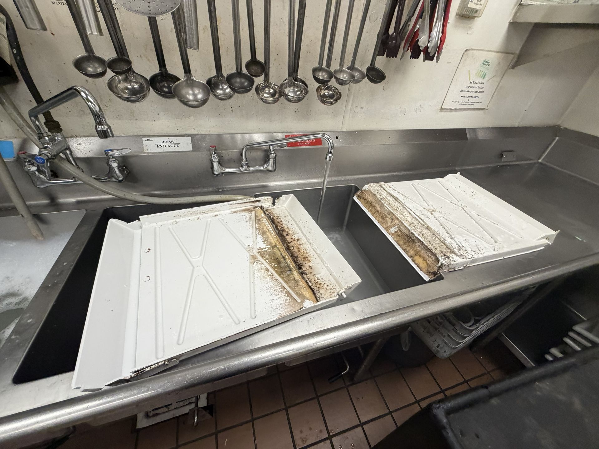 Commercial kitchen stainless prep sink with dirty inserts and hanging ladles above