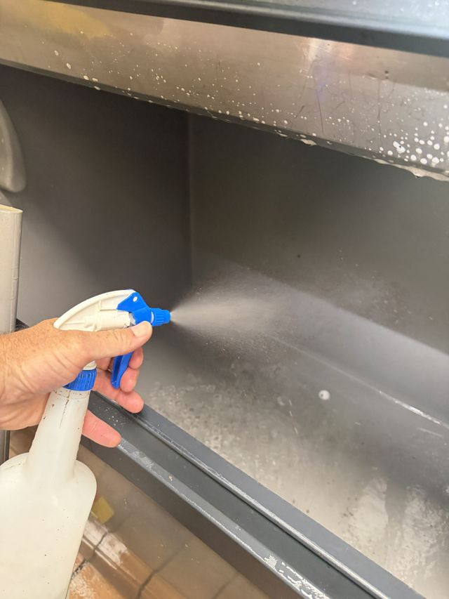 Person sprays cleaner into a metal cabinet with a white spray bottle.