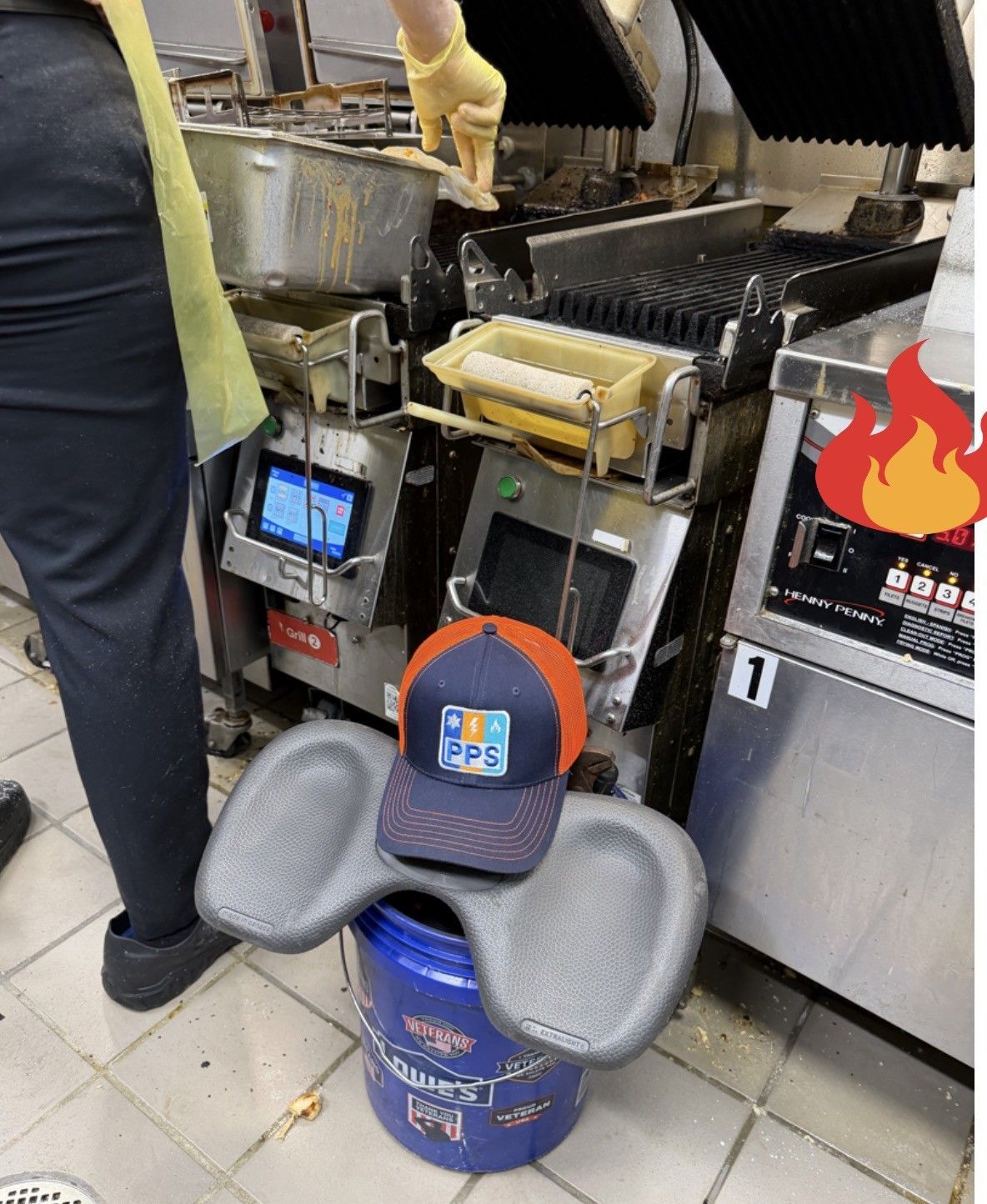 Restaurant kitchen with a hat on a bucket and a worker standing beside fryers