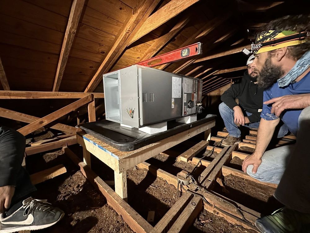 Two workers inspecting a metal box in a wooden attic with exposed beams.