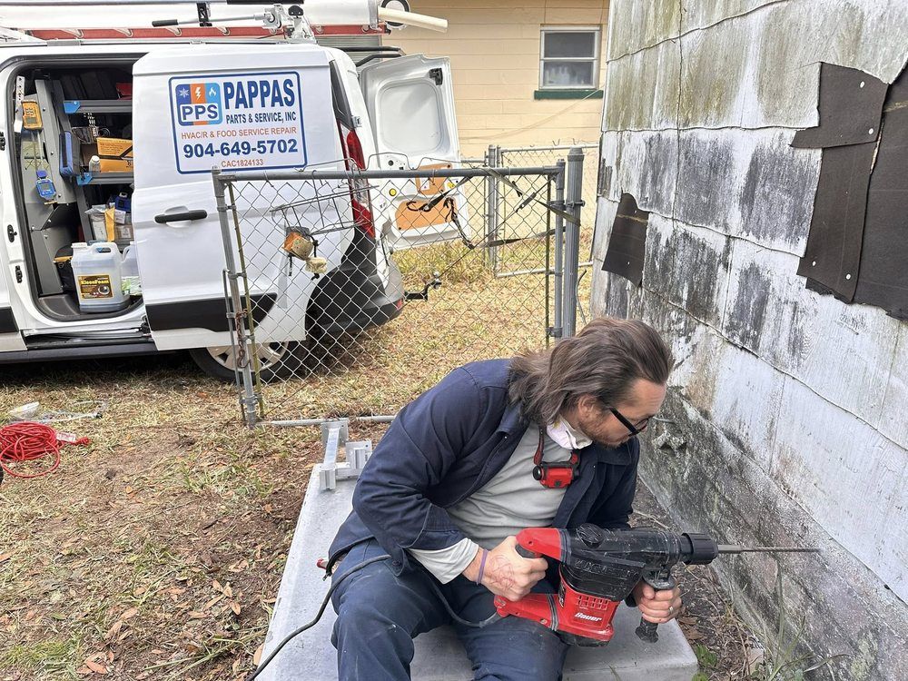 Worker using a red power saw beside a wall near a van and chain-link fence