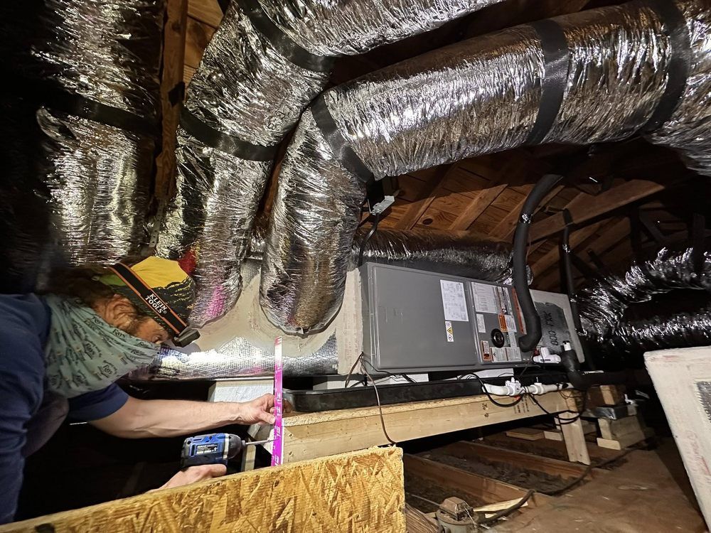 Worker inspecting HVAC ductwork in an attic with shiny insulated ducts and exposed beams
