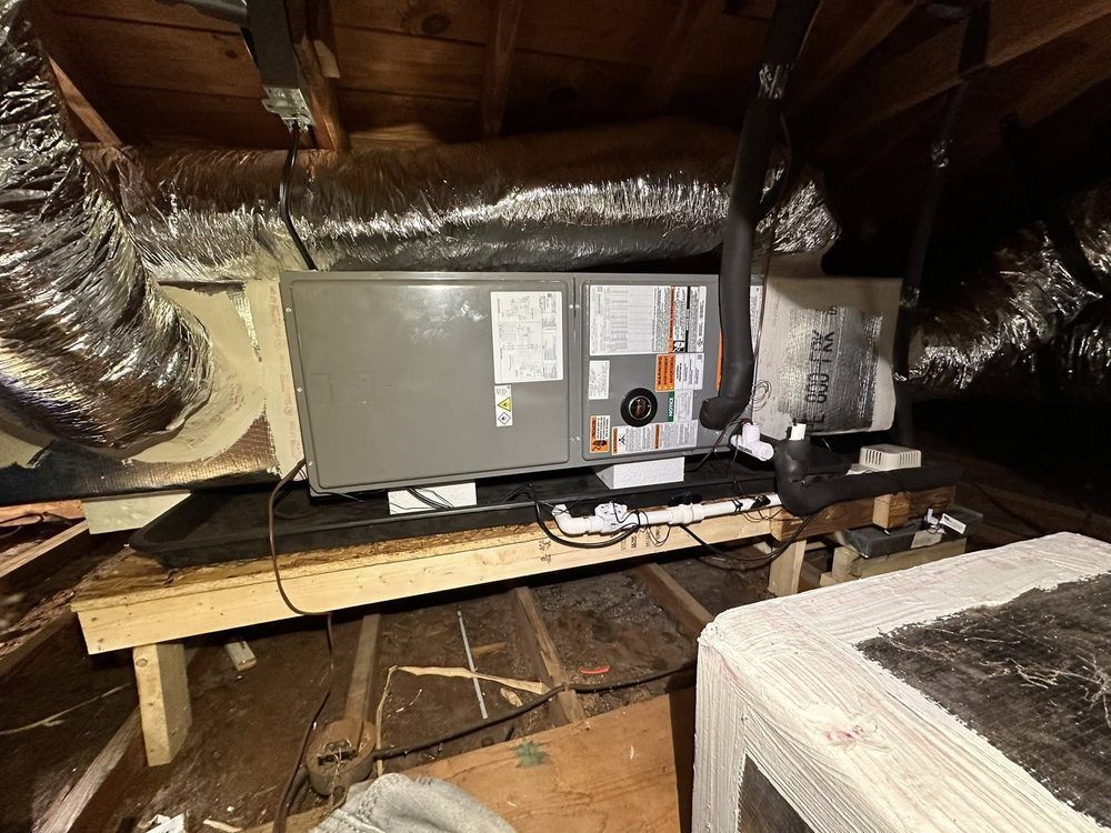 Attic HVAC unit on a wooden platform amid exposed insulation and ducts