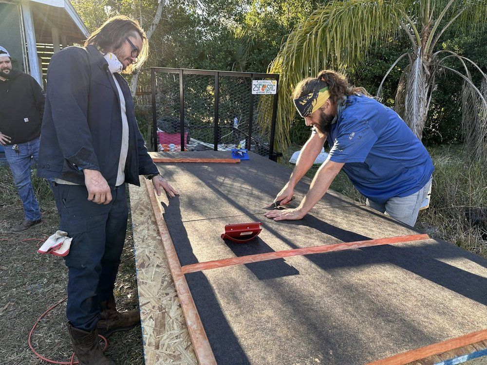 Two people measuring a tarp on the ground outdoors, with a tape measure and red tools nearby