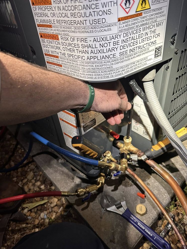 Hand adjusting valves and refrigerant lines on an outdoor HVAC unit with warning label.