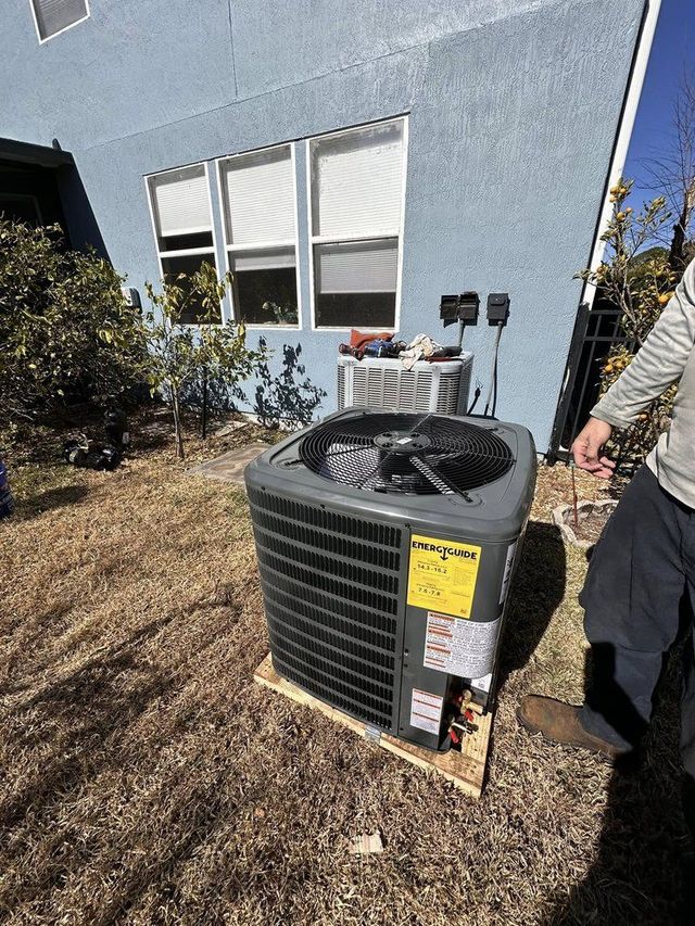 Outdoor HVAC unit beside a house, with a person standing nearby on dry grass.