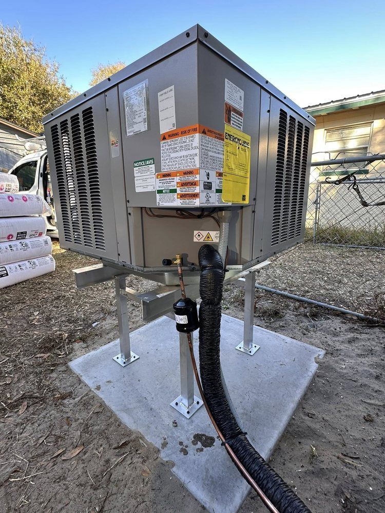 Outdoor HVAC unit on a concrete pad with black insulated hose and warning labels, beside a fence and house.