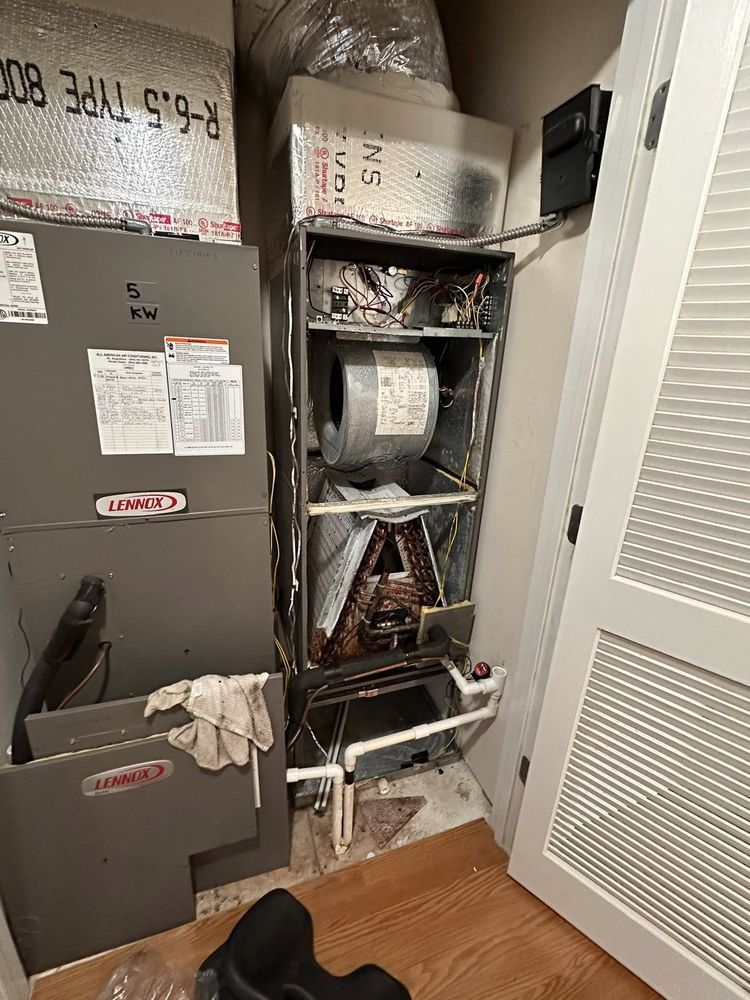 Open HVAC closet with exposed ductwork, wires, and stacked equipment beside a hallway door