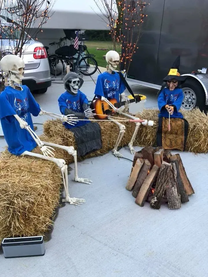 A group of skeletons are sitting around a fire pit.