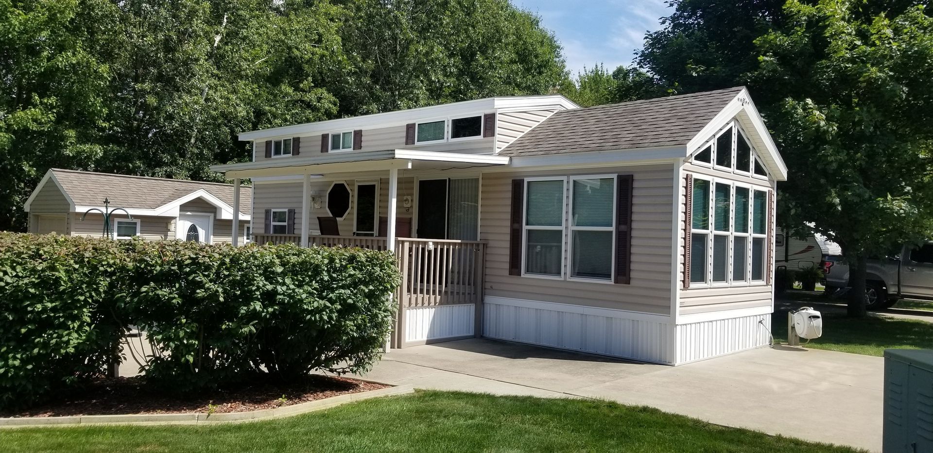 A mobile home with a large porch is sitting on top of a lush green lawn.