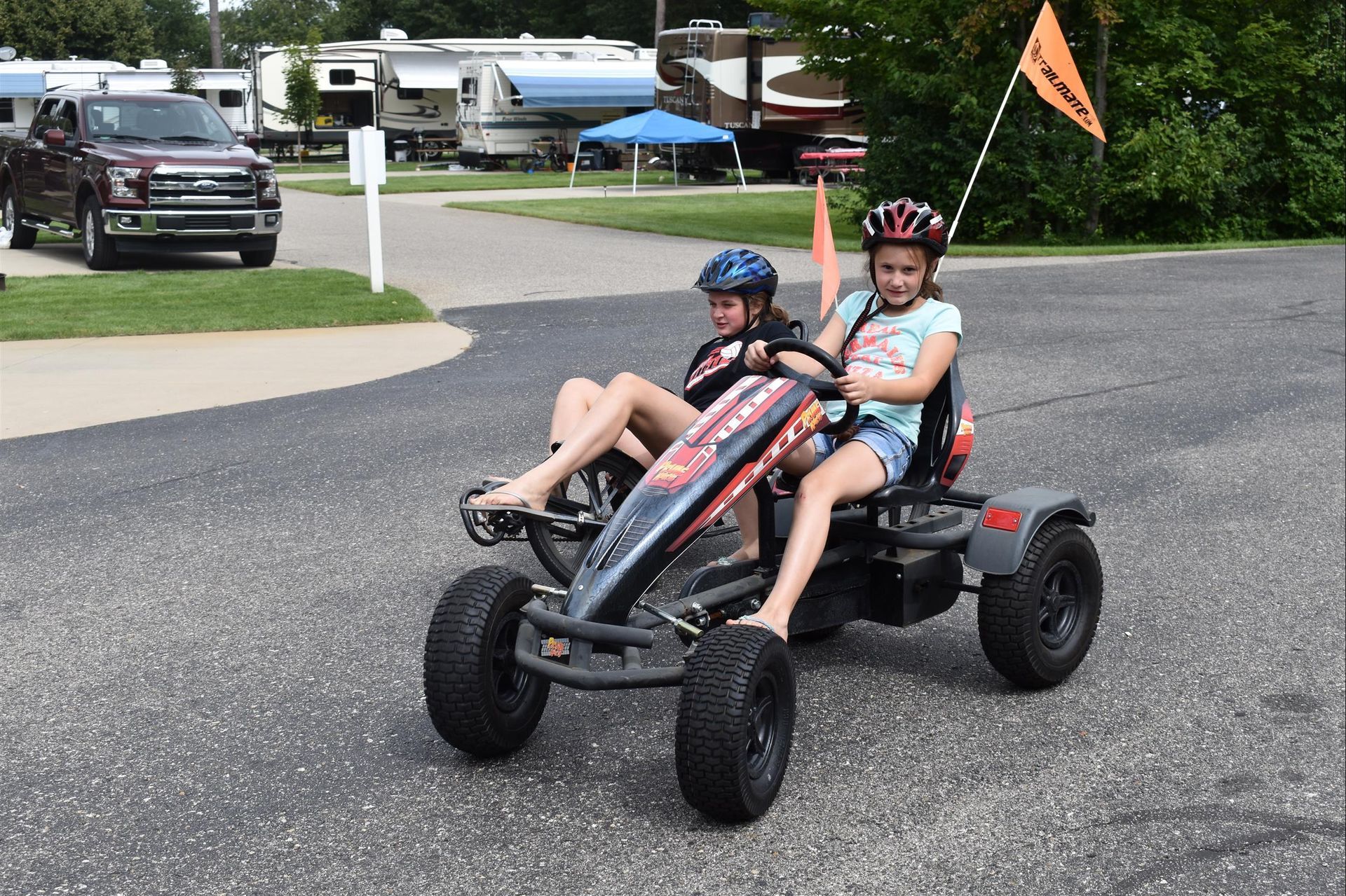 Two children are riding a go kart on a road.