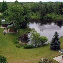 An aerial view of a house next to a lake surrounded by trees.