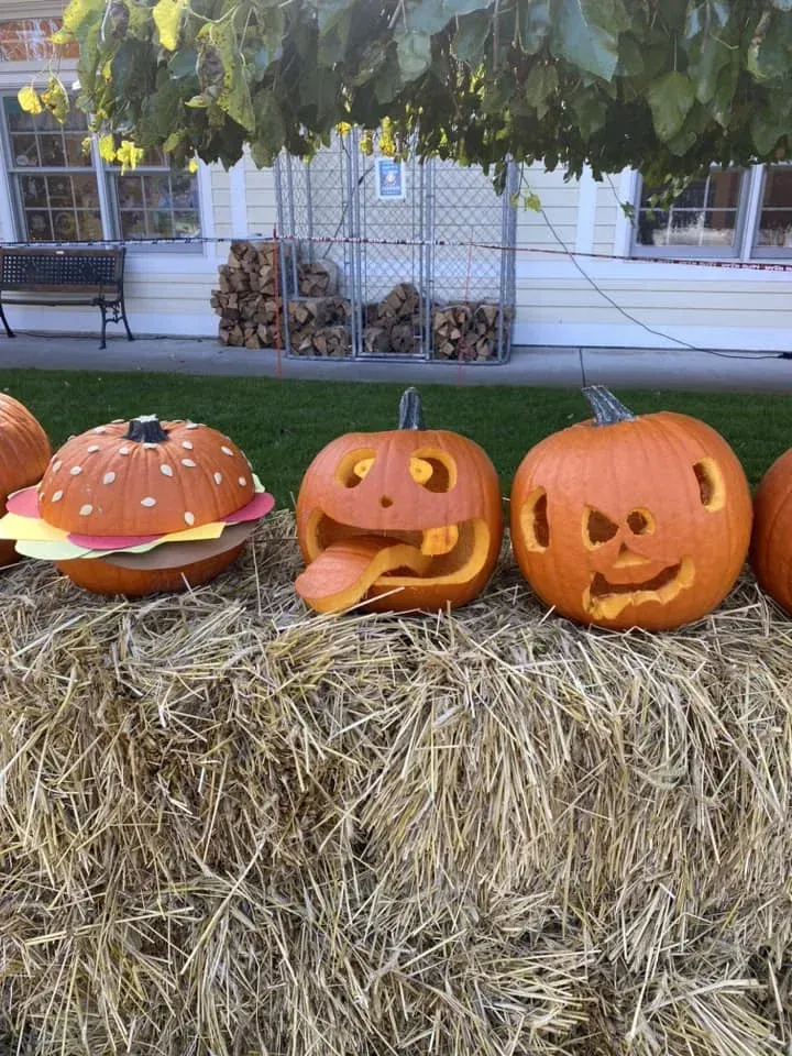 A bunch of pumpkins carved to look like hamburgers are sitting on a bale of hay.