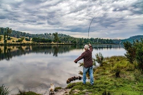 A man is fishing in a lake with a dog.