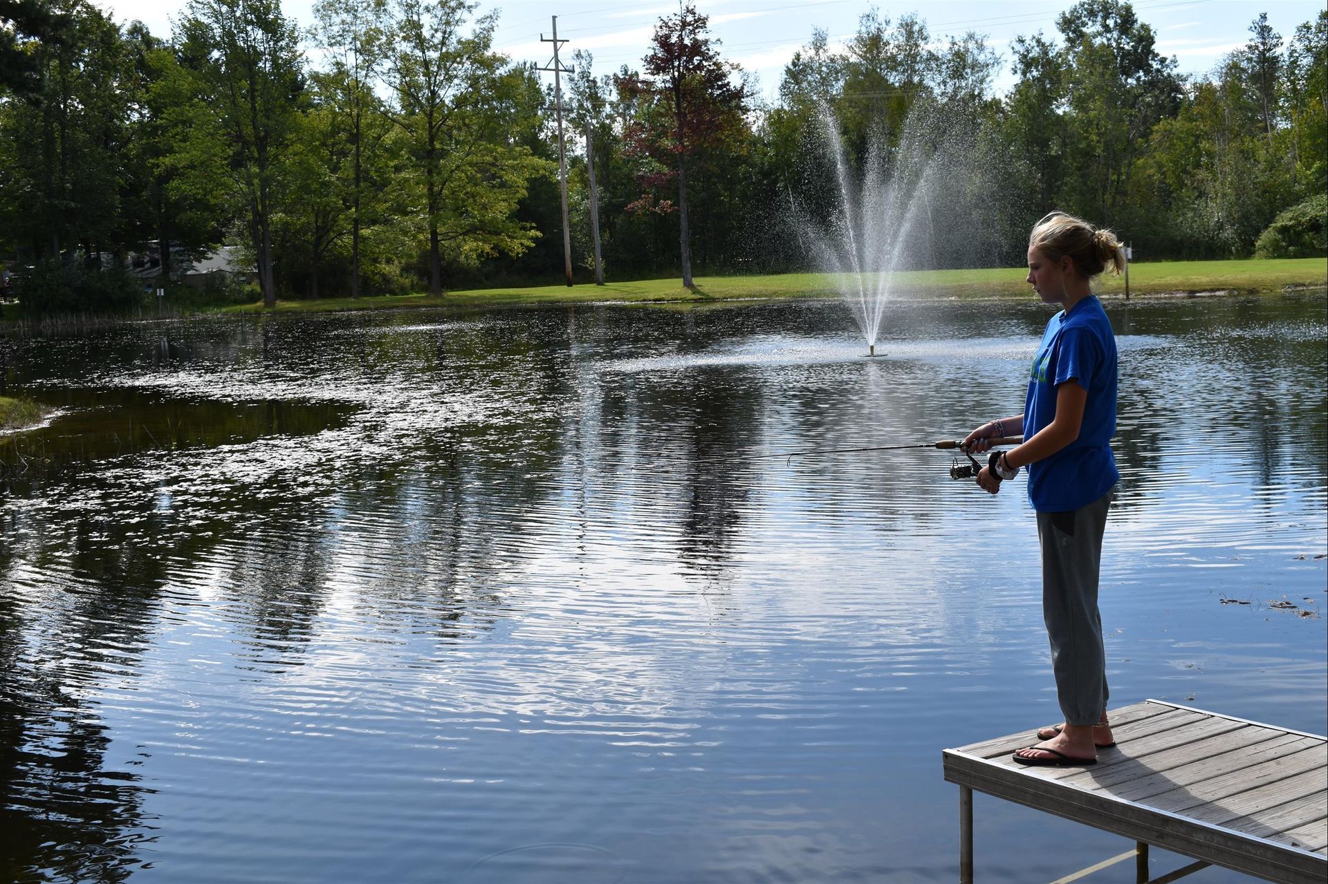 A girl is standing on a dock near a pond holding a remote control