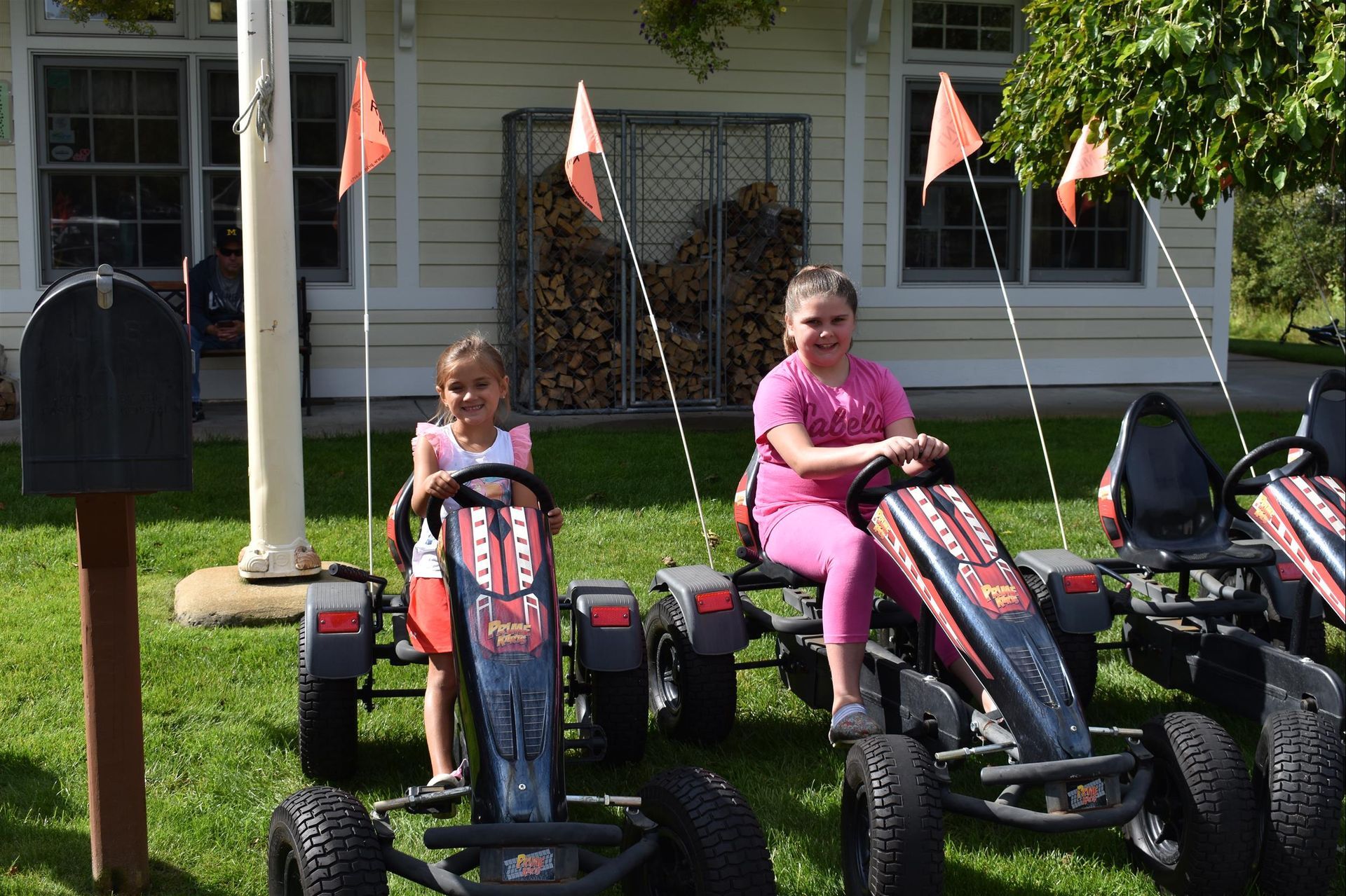 Two girls are riding go karts in front of a house