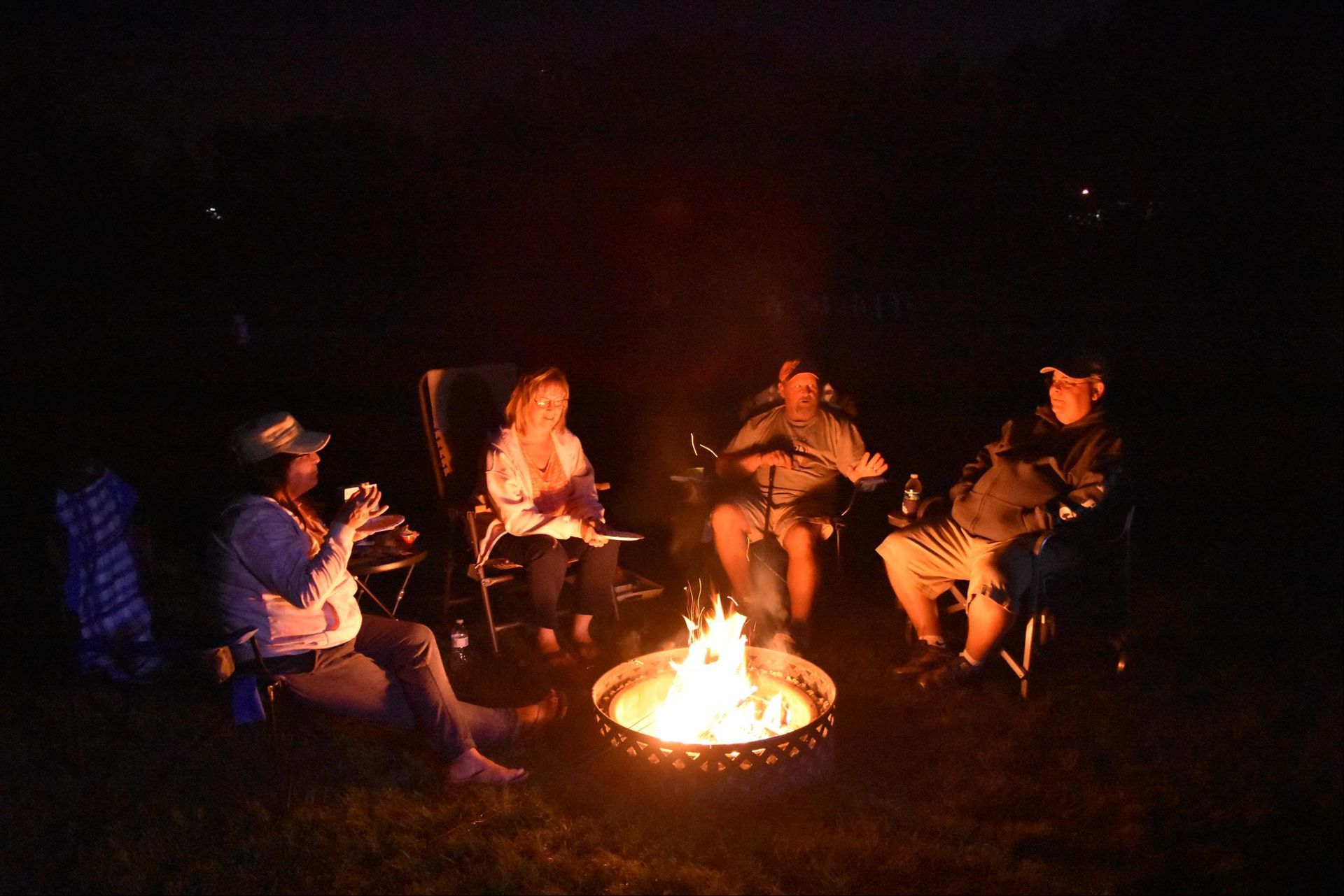 A group of people are sitting around a fire pit at night.