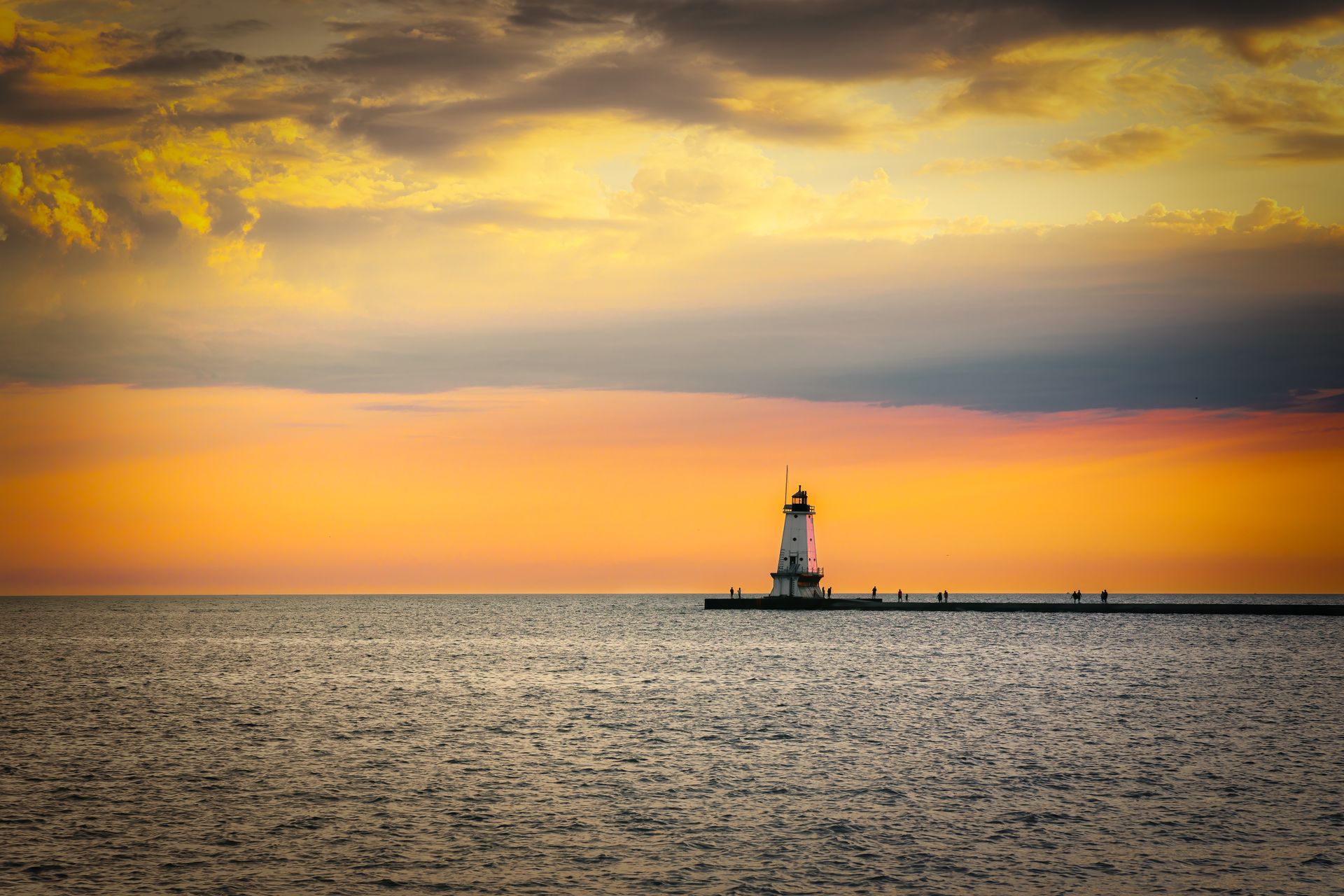 A lighthouse in the middle of the ocean at sunset.