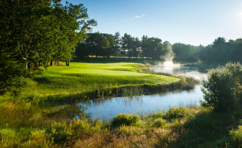 A golf course with a lake and trees in the background.