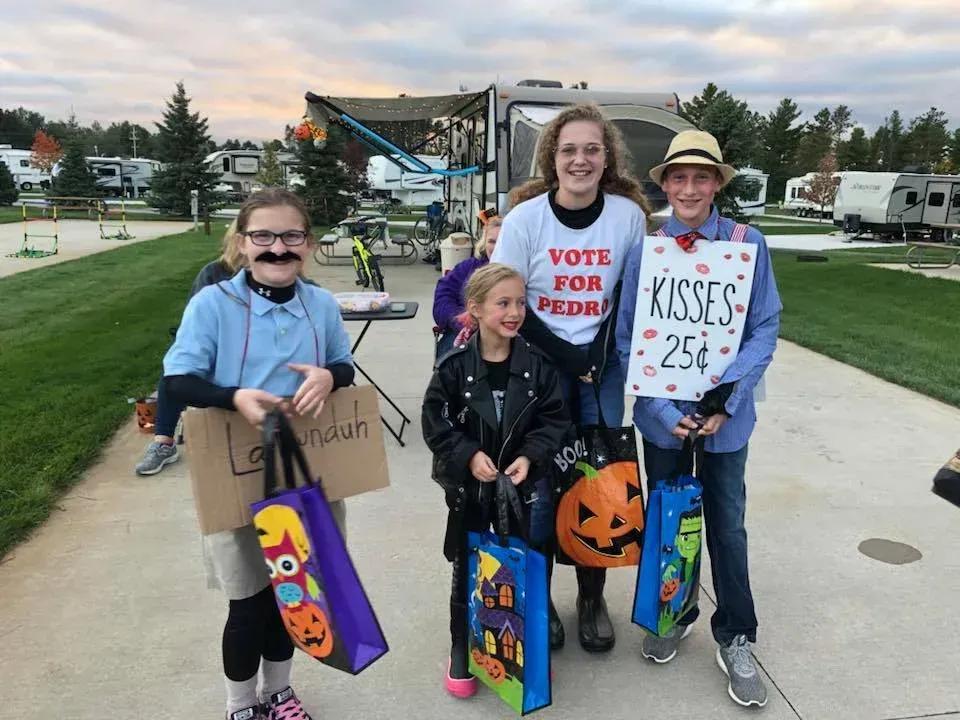 A group of children are standing on a sidewalk holding trick or treat bags.