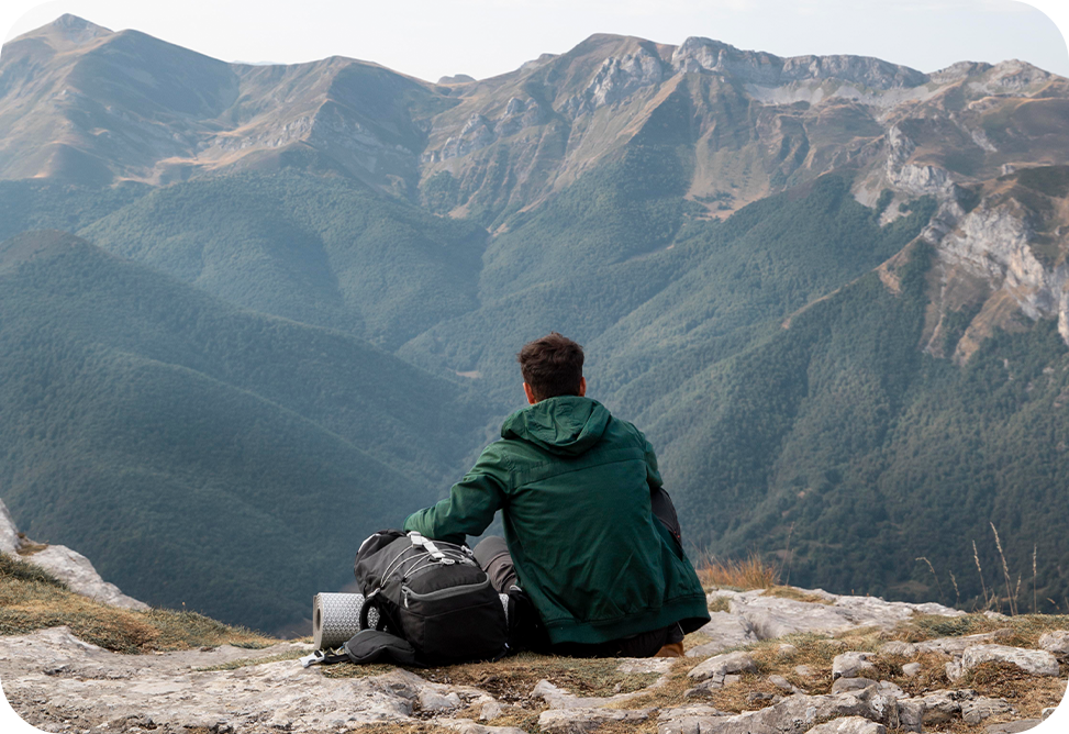 A man with a backpack is sitting on top of a mountain.