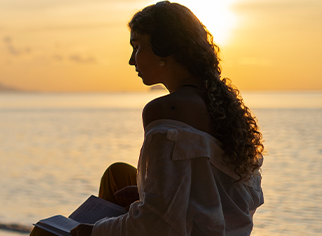 A woman is sitting on the beach reading a book at sunset.