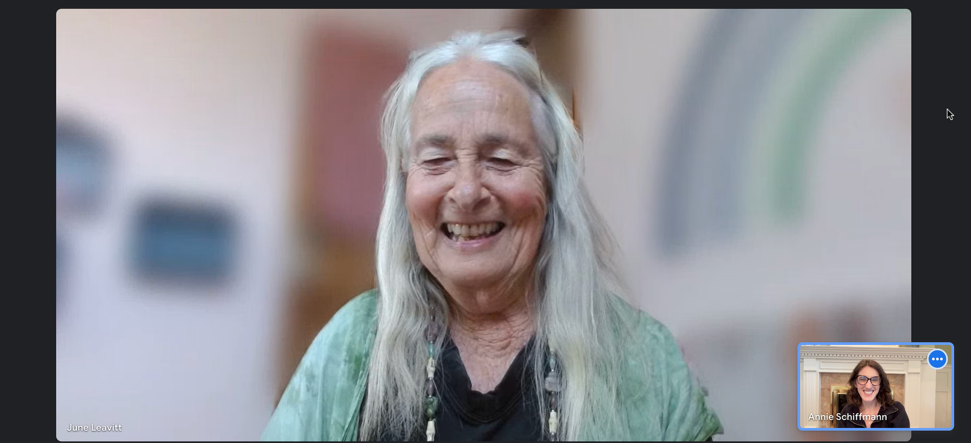 A woman with long white hair is smiling on a video call.