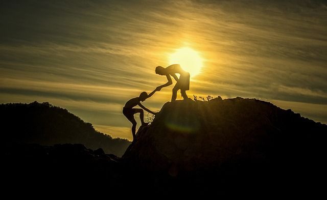 One person helping another.  Man helping another man up a mountain