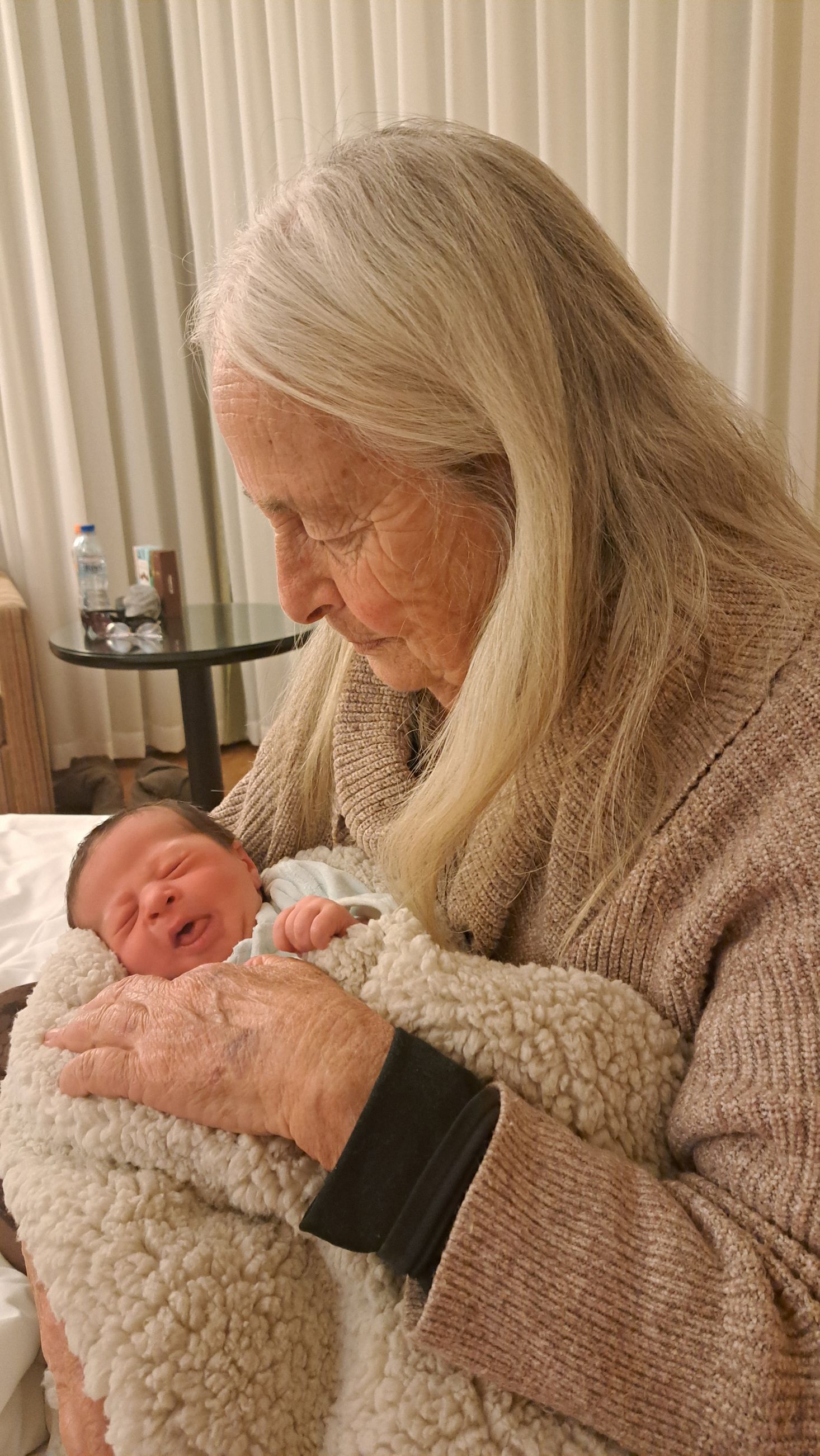 White-haired woman holding a newborn baby. Grandmother with a new grandchild