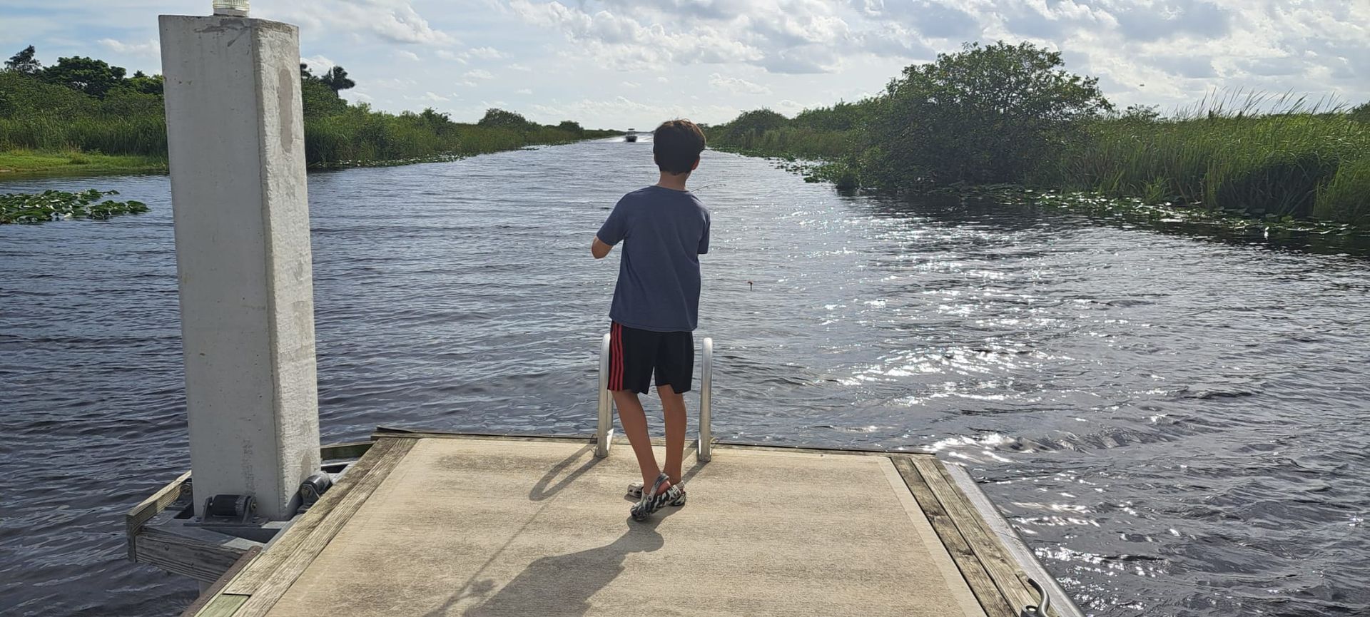 A young boy is standing on a dock overlooking a body of water.