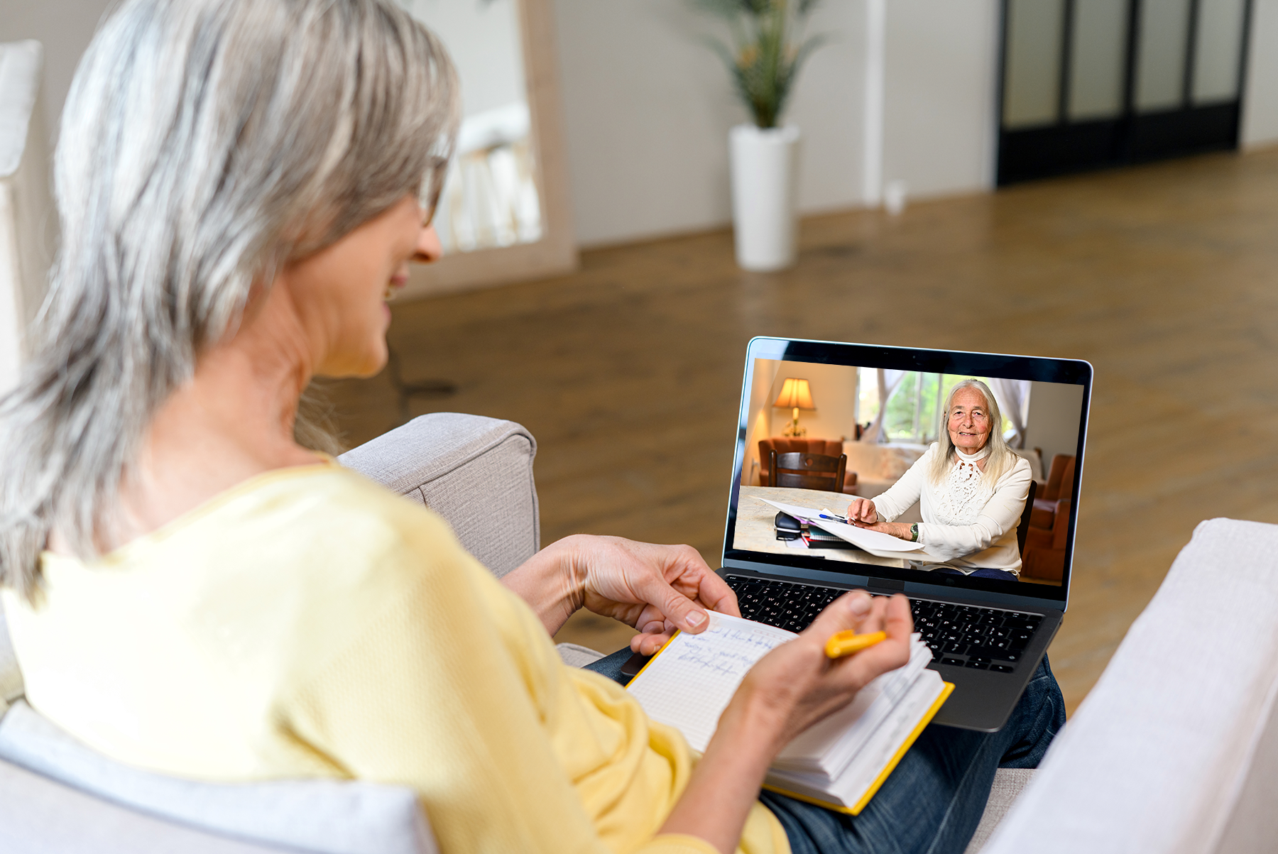 An older woman is sitting on a couch using a laptop computer.