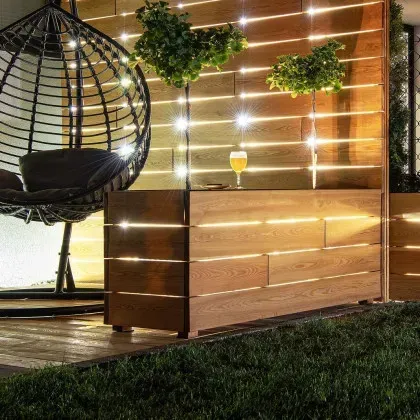 Outdoor wooden bar with string lights, hanging chair, and green plants.