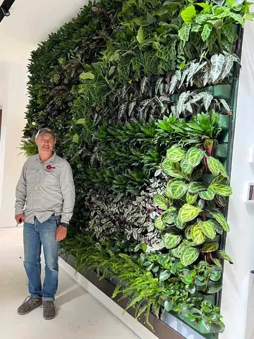 Man standing next to a large vertical garden wall with various green plants.