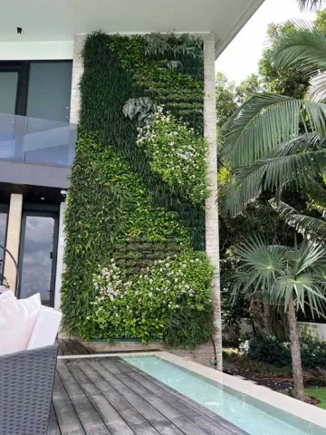 Vertical garden on a building facade with lush greenery, next to a pool and wooden deck.