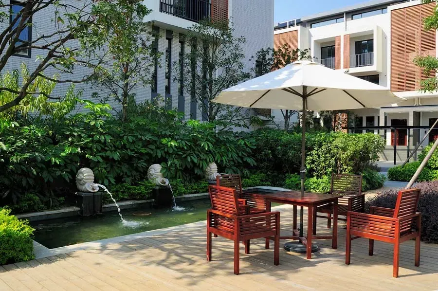 Outdoor seating area with table, chairs, umbrella, water feature, and building backdrop.