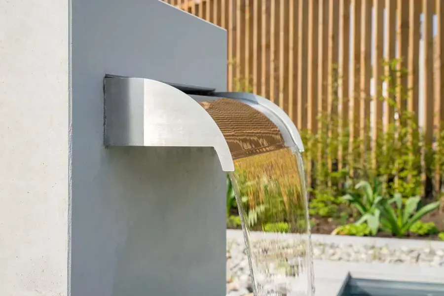 Modern outdoor water fountain with clear water cascading from a brushed metal spout.