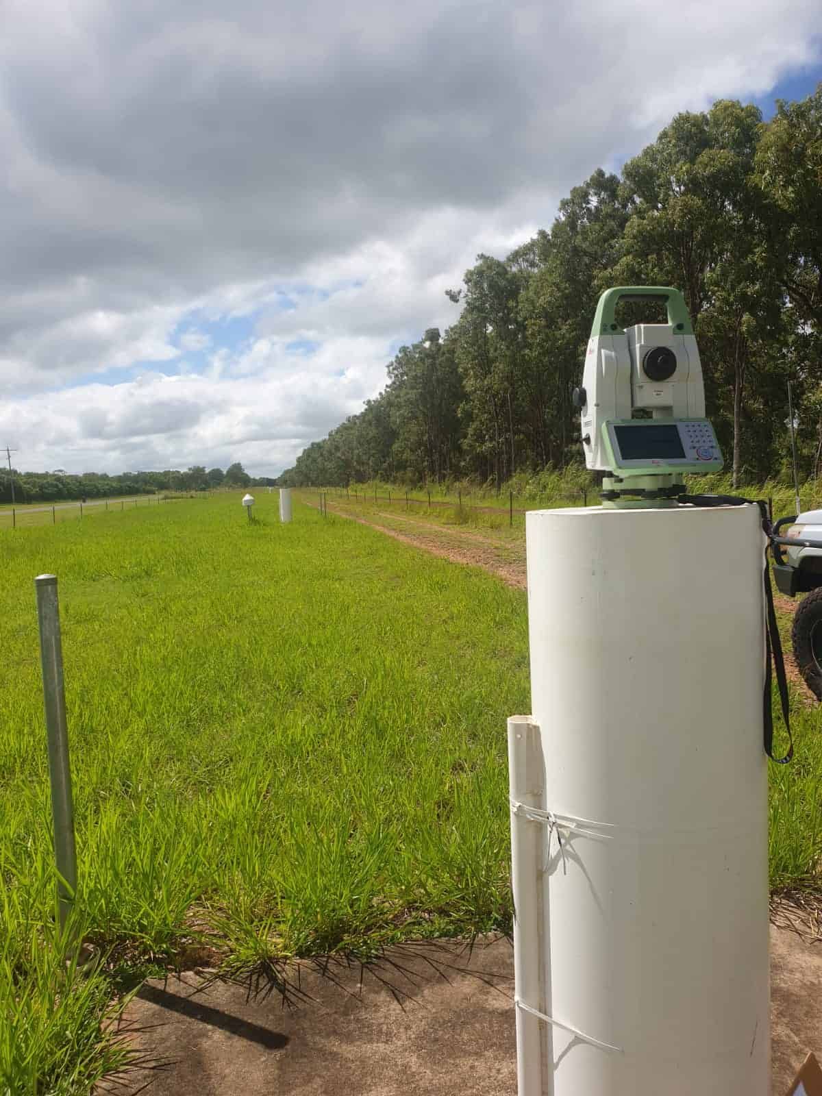 A Total Station Is Sitting On Top Of A White Pipe In A Field — TerraModus Surveying In Bayview Heights, QLD