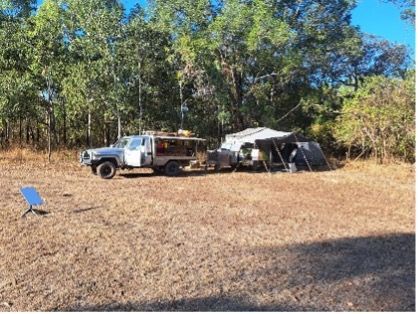 Camping scene: A truck and trailer with a tent set up in a dry, grassy area surrounded by trees.