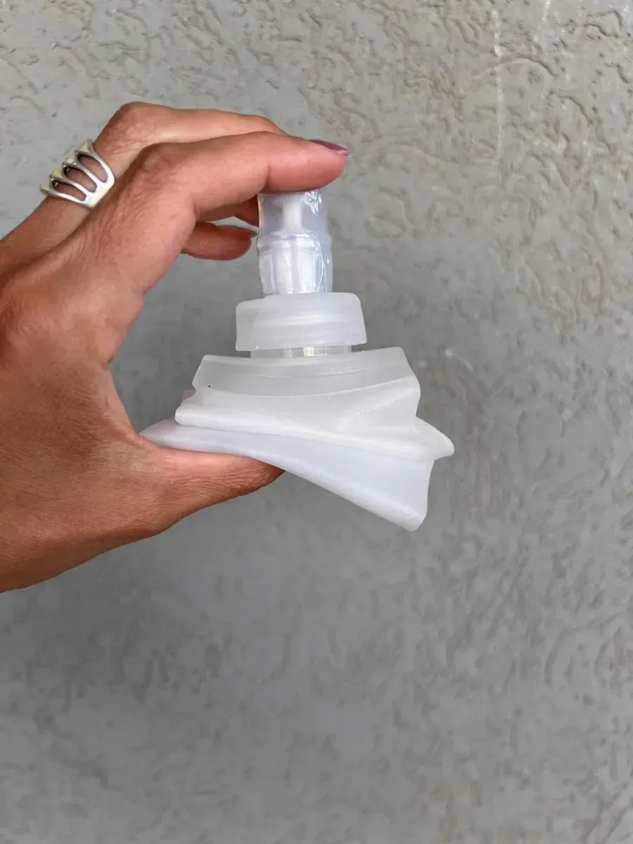 Dos botellas transparentes y plegables descansan sobre un poste de madera contra un fondo de sendero de montaña.