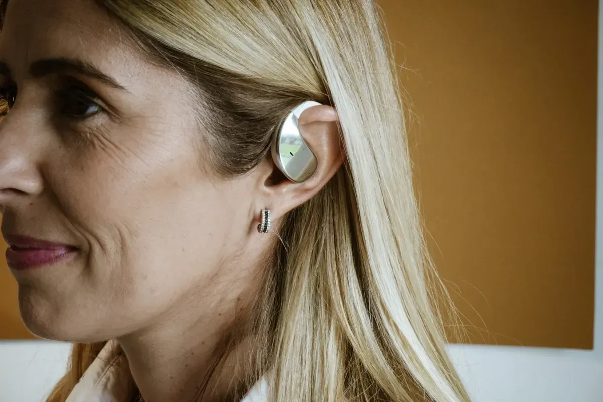 Auriculares con gancho para la oreja y estuche de carga. Grises y plateados con pantalla digital.