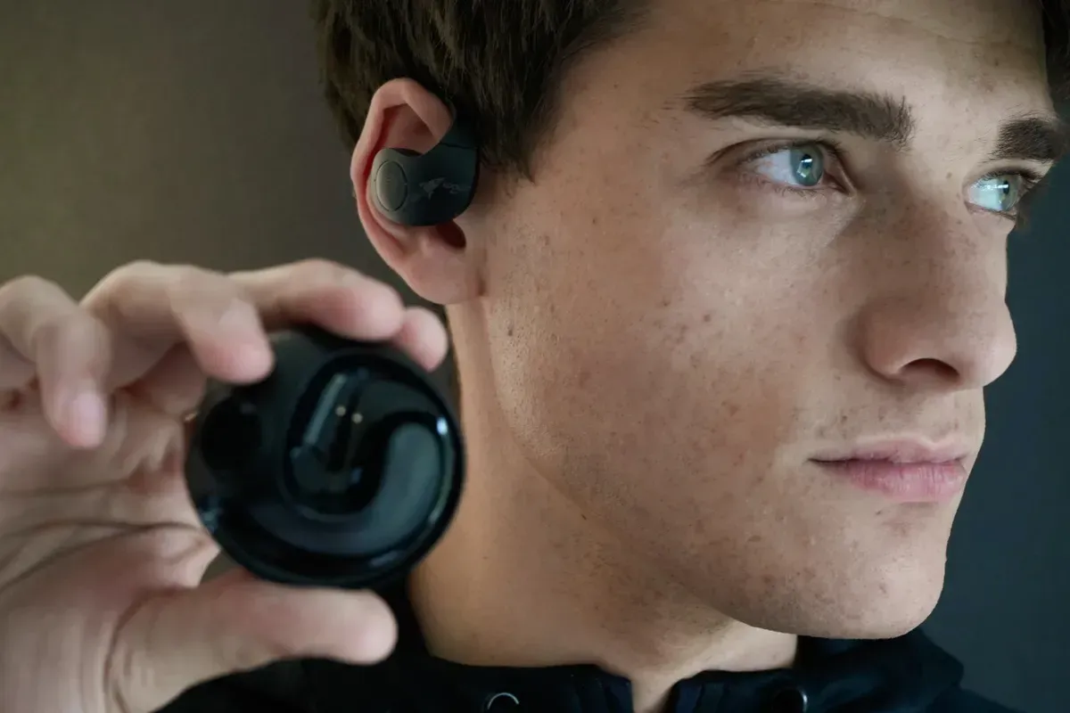 Auriculares inalámbricos negros con estuche de carga; los auriculares tienen ganchos para la oreja.