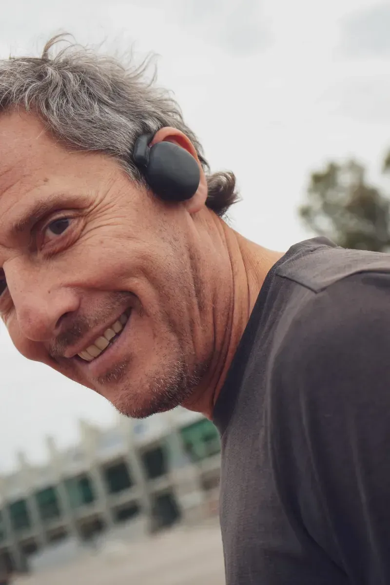 Auriculares deportivos inalámbricos negros con ganchos supraaurales y luces indicadoras de carga.