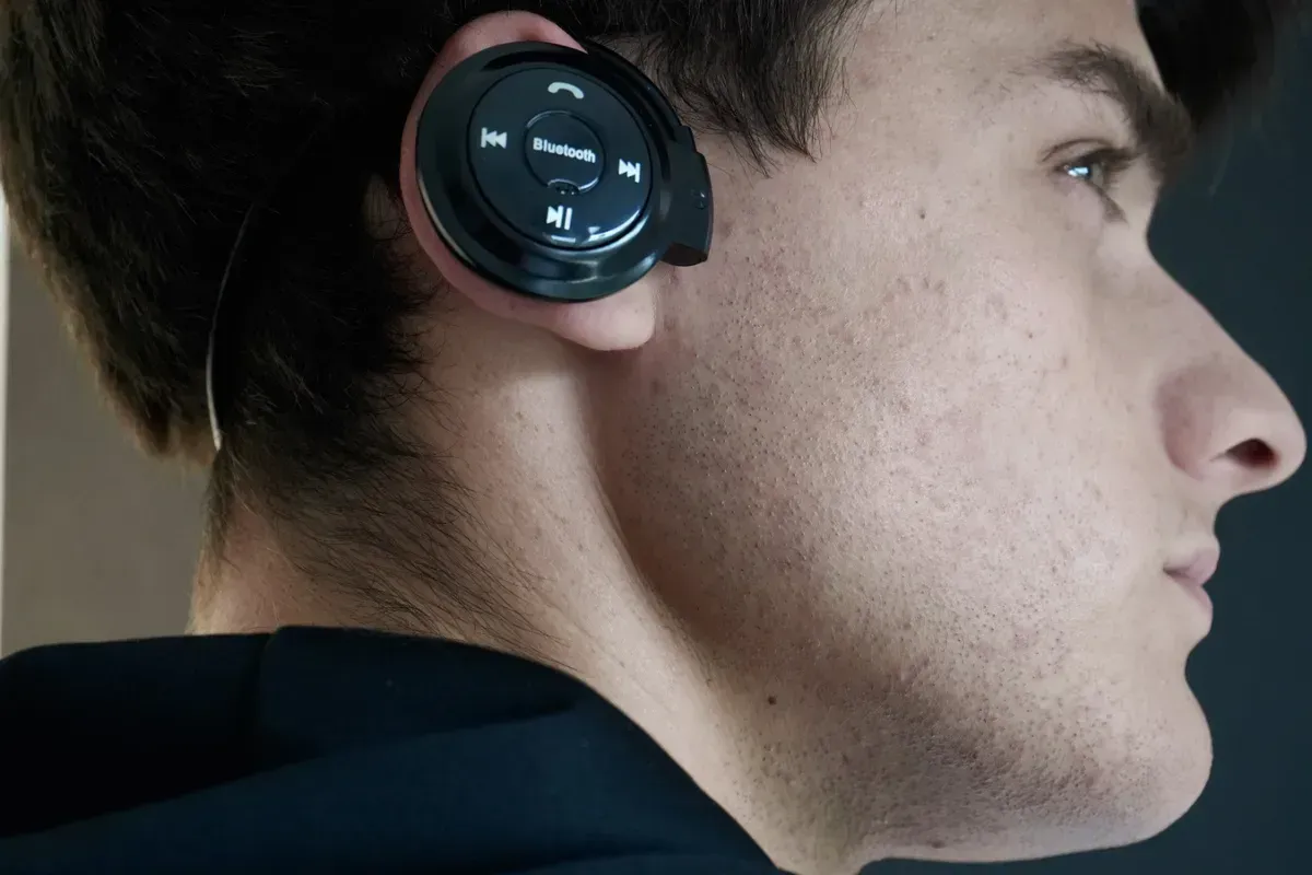 Auriculares Bluetooth negros con presillas para las orejas y controles visibles en los auriculares.