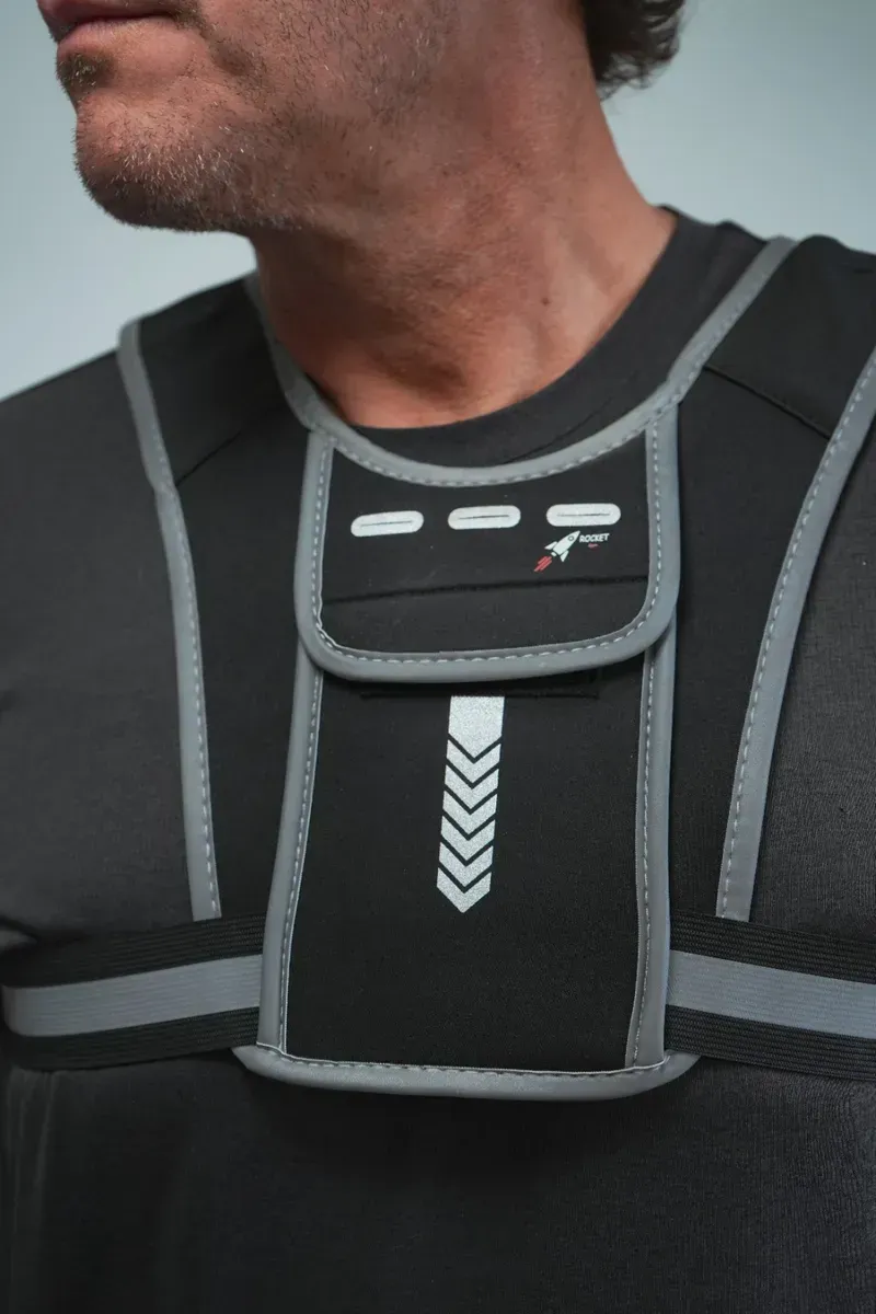 Hombre que lleva un arnés de pecho negro con ribete gris reflectante y un bolsillo central.